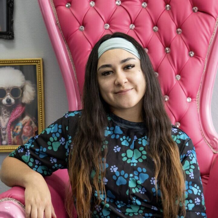 Smiling woman sitting on a luxurious pink chair with a floral dress.